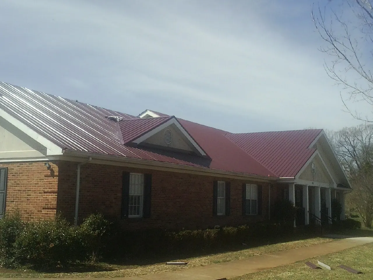 Red metal roof with gabled entries on a long brick building, from a Hail Damage Roof Repair job in Warsaw